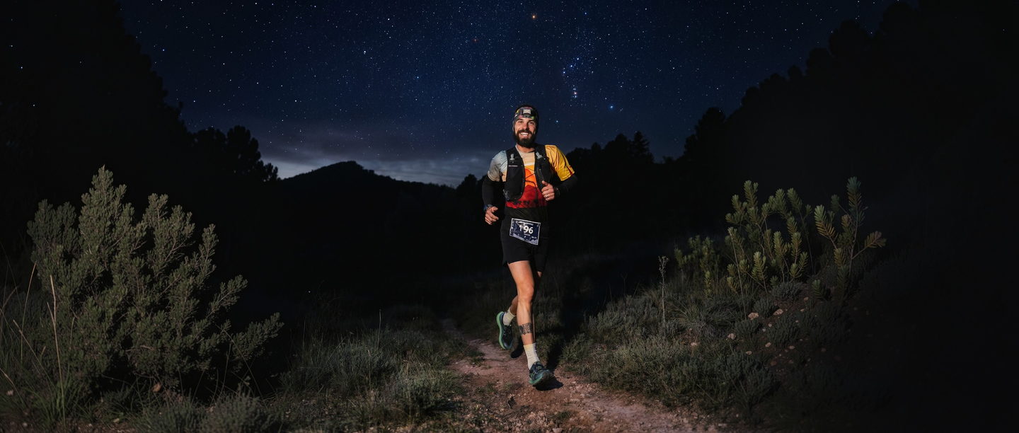 Un corredor con frontal por un sendero de matorral bajo un cielo lleno de estrellas